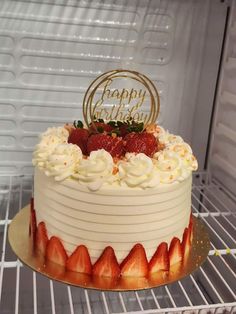 a birthday cake with white frosting and strawberries on top is sitting in an open refrigerator