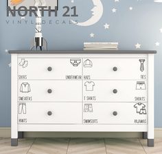 a white dresser sitting in front of a wall with stars and moon decals on it