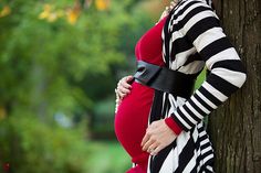 a pregnant woman leaning against a tree