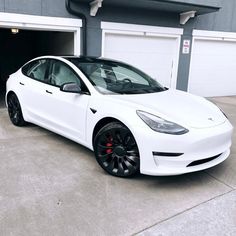 a white tesla parked in front of a garage