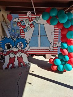 there is a birthday sign and balloons on the ground in front of a building with an image of dr seuss