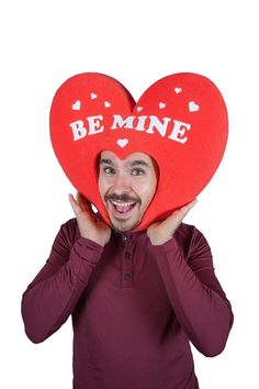 a man holding two red heart shaped cushions with the words be mine on them in front of his face