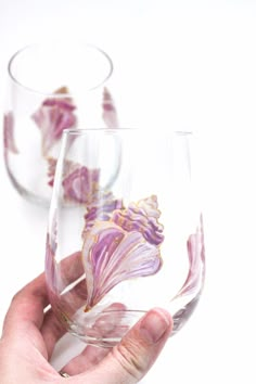 two hand painted wine glasses being held up by someone's left hand, on a white background