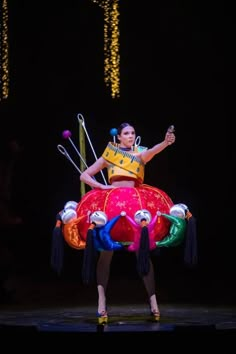 a woman is dancing on stage with some balloons and sticks in her hand while wearing a yellow shirt