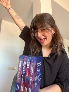 a woman is holding three books in her hands and smiling at the camera with both arms up