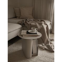 a coffee table with books and a cup on it in front of a couch that is covered by a blanket