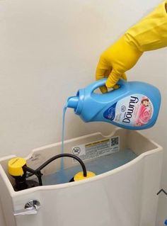 a person in yellow gloves is pouring water into a toilet with a blue canister