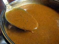 a spoon full of brown liquid sitting on top of a glass bowl filled with food