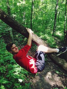 a man is hanging from a tree in the woods with his feet up on it