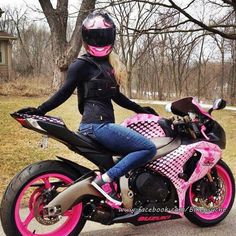 a woman sitting on top of a pink and black motor bike in the street next to some trees