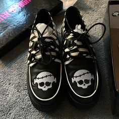 a pair of black and white shoes with skull decals on them next to a box