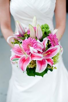 a bride holding a bouquet of pink and white lilies in her wedding day dress