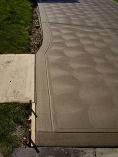 a concrete walkway with grass and bushes in the backgroung, next to a house