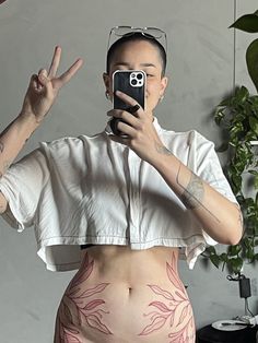 a woman taking a selfie with her cell phone in front of her belly and tattoos on her stomach