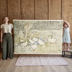 two girls standing next to a painting with ducks on it and one girl holding the frame