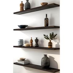 three wooden shelves with vases and other items on them in a white walled room