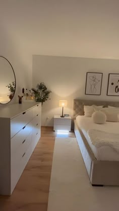 a large white bed sitting in a bedroom next to a dresser and mirror on top of a hard wood floor