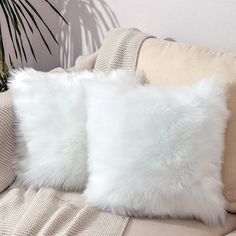 two white fluffy pillows sitting on top of a couch next to a potted plant