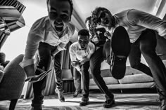 three men are playing with a skateboard in the living room while another man looks on