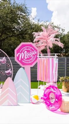 pink and white decorations are on the table in front of a fence with palm trees