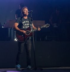 a man singing into a microphone while holding a guitar in front of him on stage