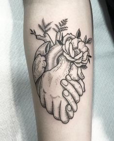 a black and white tattoo of two hands holding a heart with flowers on it's side