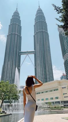 a woman standing in front of two tall buildings with water spouting from them