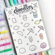 an open notebook with doodles on it next to some markers and pencils in the background