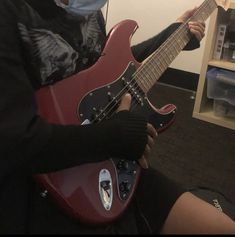 a person wearing a face mask and holding a red guitar in their hand while sitting on the floor