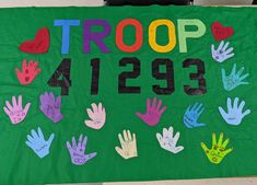 a group of children's handprints on a green sign that says troop