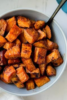 a bowl filled with cooked sweet potatoes on top of a white tablecloth next to a spoon