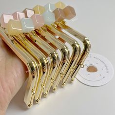 a hand holding a bunch of gold colored hair clips on top of a white table