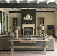 a living room with couches and a table in front of a fireplace that has chandelier above it