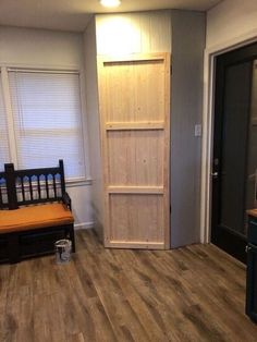 an empty room with wood floors and a wooden door in the corner, next to a bench