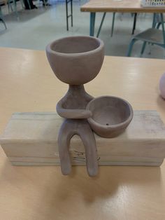 a clay sculpture sitting on top of a wooden table next to a bowl and spoon