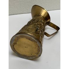 an old brass wine glass sitting on top of a white table next to a wall