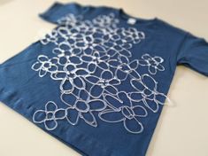 a blue t - shirt with silver wire work on the front and back, sitting on top of a table