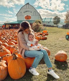 a woman holding a baby sitting on top of a pumpkin patch