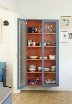 a blue china cabinet with dishes on it in a room that has white walls and wood floors