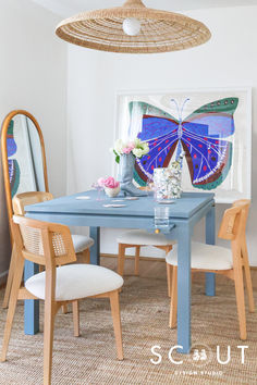 a blue table and chairs in a room with a butterfly painting on the wall behind it