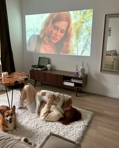 a woman laying on the floor in front of a tv with two dogs sitting next to her