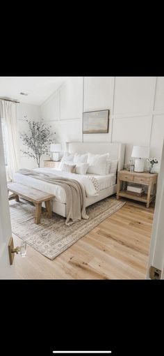 a large white bed sitting in a bedroom on top of a hard wood floor next to a window