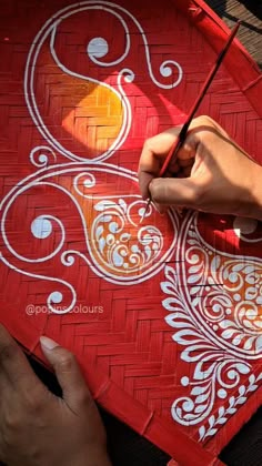 someone is drawing on a piece of red paper with white designs and oranges in the background