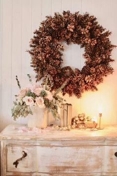 a white dresser topped with a wreath and flowers next to a lit candle on top of it