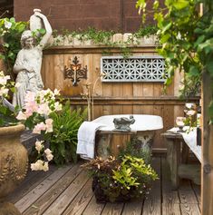 an outdoor bathtub surrounded by potted plants and other greenery in front of a wooden fence