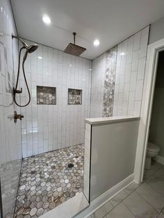 a bathroom with white tile and hexagonal floor tiles on the walls, shower head, and toilet