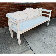 a white bench sitting on the sidewalk next to a brick wall in front of a building