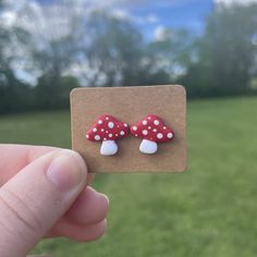 a hand holding up a small red and white mushroom studs on top of a piece of cardboard