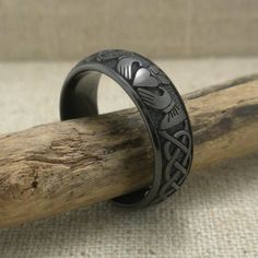 a black ring with an intricate design on it sitting next to a piece of wood