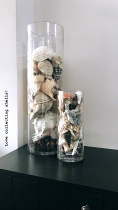 two vases filled with shells on top of a black table next to each other